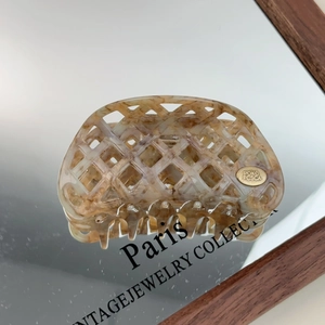 Detail of amber marble acetate hair claw with hollow waffle pattern and gold logo