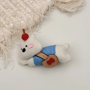Close-up of white plush bear with blue vest and cherry hair pin on beige knit background