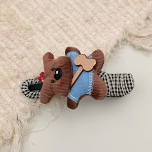 Close-up of brown corduroy teddy bear hair clip with blue vest on checkered fabric base