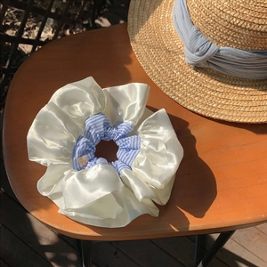 Detail of blue plaid oversized satin scrunchie with handmade tag on a sunlit wooden table