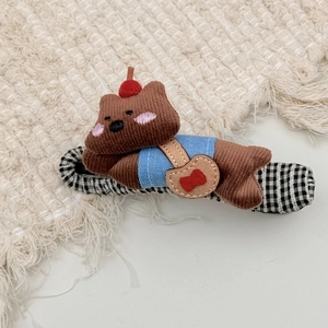 Detail of cute plush bear hair claw with blue shirt and brown bag on checkered fabric