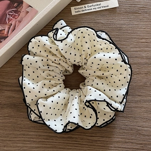 Elegant white polka dot scrunchie with black trim on a rustic wooden table