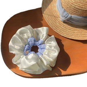 Oversized blue plaid and cream satin scrunchie displayed on a wooden tray with a straw hat
