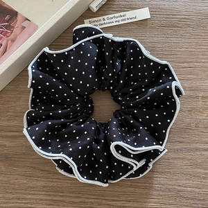 Polka dot scrunchie with white scalloped edges on a wooden surface with lifestyle props