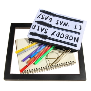 White canvas cosmetic bag with black slogan and zipper on office stationery background