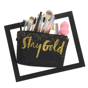 Black canvas cosmetic bag with Stay Gold gold print filled with makeup brushes and sponges