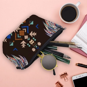 Travel makeup bag with geometric tribal patterns and colorful feather art on pink desk
