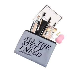 Gray canvas cosmetic bag with bold lettering and makeup essentials on white background