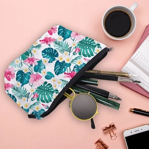 Floral makeup bag with pink hibiscus and palm leaves on pink background with accessories