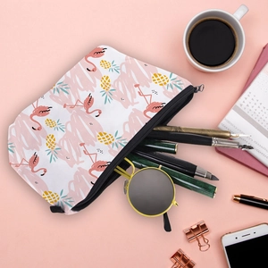 Cosmetic bag with pink flamingo and pineapple print on a pink desk with accessories