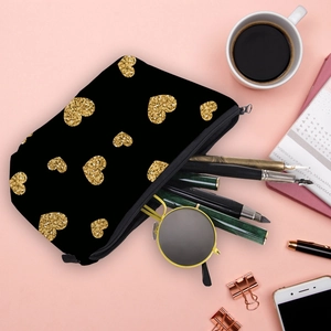 Black cosmetic bag with gold heart prints and zipper, shown with travel accessories