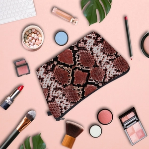 Flat lay of snakeskin print pouch with cosmetic accessories on pink background