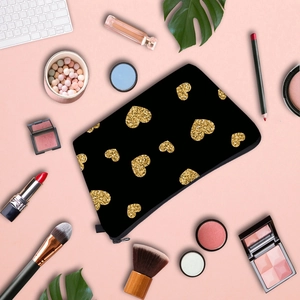 Cosmetic bag with gold glitter heart pattern on pink background with makeup tools