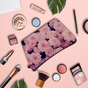 Flat lay of rose print travel makeup bag with cosmetics on a soft pink background