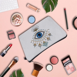 Flat lay of gray Evil Eye makeup bag with cosmetics on pink background, stylish travel pouch