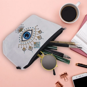 Flat lay of Evil Eye makeup bag with sunglasses, pens and stationery on pink surface