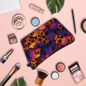 Flat lay of skull print makeup bag surrounded by beauty brushes and cosmetics on pink background