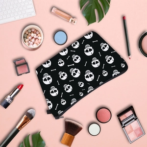 Flat lay of stylish skull print makeup bag with black zipper on creative pink workspace