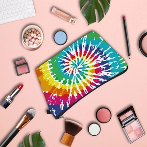 Flat lay of colorful rainbow tie-dye makeup bag with cosmetics on pink background