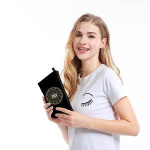 Close-up of a black waterproof makeup bag with a gold zodiac print held by a model