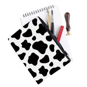 Detail view of square cow print makeup bag with black zipper on creative office desk