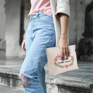Linen style makeup bag with floral print wreath and outta here text held by a model