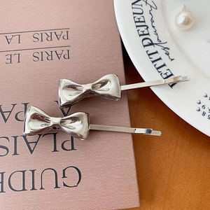 Detail of two silver metal bow hair clips with polished finish on a French-style table