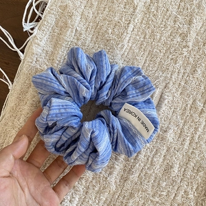Détail d'un chouchou en tissu à rayures bleues avec étiquette Made in Korea et lin