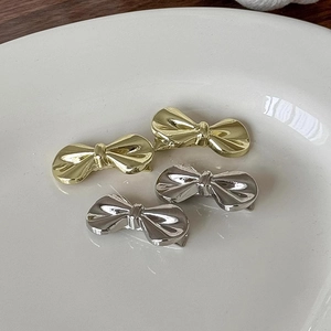Set mit vier Metall-Haarspangen in Schleifenform in Gold und Silber auf einem Teller