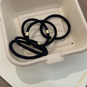 Detail of high-elastic black hair ties with minimalist gold metal buckles in a box