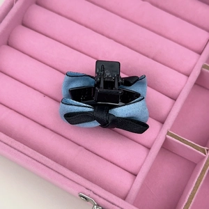 Détail d'une pince à cheveux avec nœud en tissu bleu et noir sur velours rose