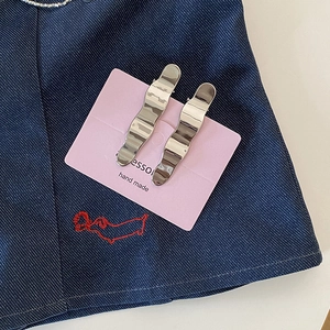 Détail de pinces à cheveux ondulées en métal argenté brillant sur carte rose