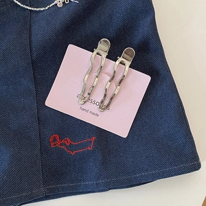 Détail de deux barrettes ondulées argentées sur carte rose sur fond de tissu en denim