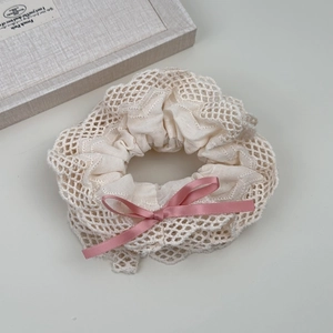 Close-up of cream lace scrunchie with pink satin bow and fine mesh texture detail