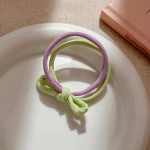 Close-up of pastel purple and green elastic hair ties with bow detail on a white plate