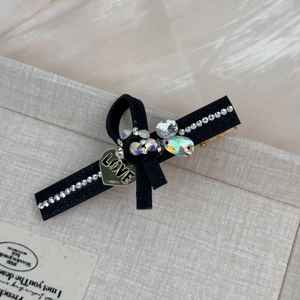Détail d'une pince à cheveux en cuir noir ornée de strass et d'un pendentif coeur LOVE