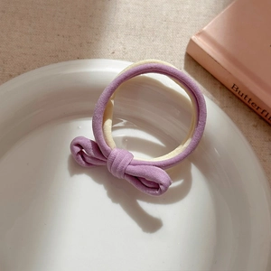 Detail of high-elastic purple and cream bow hair tie on a white decorative plate