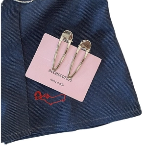 Lot de barrettes à cheveux minimalistes en métal argenté sur carte rose et fond en denim bleu