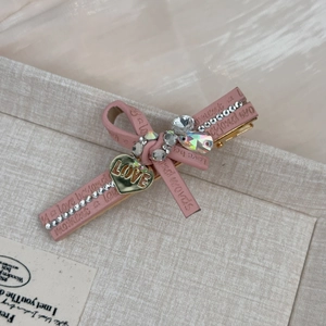 Pince à cheveux noeud rose avec texture cuir, breloque coeur dorée et strass brillants