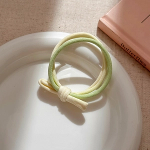 Close-up of yellow and green elastic hair ties with knot detail on a ceramic dish