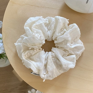 Détail d'un chouchou blanc crème avec texture rayée et bordure de petits pompons