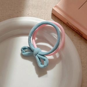 Detail of high-elasticity blue bow and pink circular hair ties in a ceramic dish