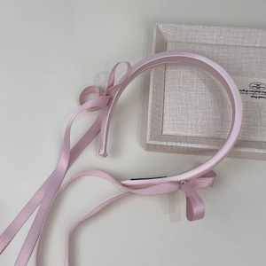 Close-up of pink satin headband with long ribbon bow on a textured beige tray