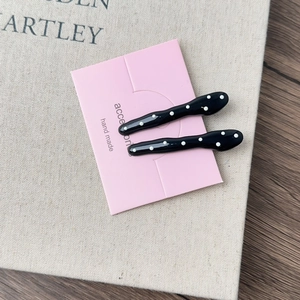 Detail of French black and white polka dot hair clips on a pink accessories display card