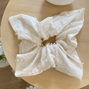 Chouchou élégant en tissu blanc crème avec broderie ondulée sur un tabouret en bois