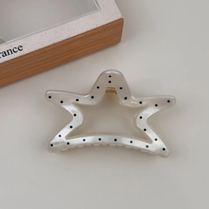 Macro detail of star-shaped hair claw clip with black polka dots and gold spring