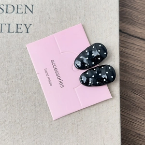 Close-up of black and white polka dot oval stud earrings on pink presentation card