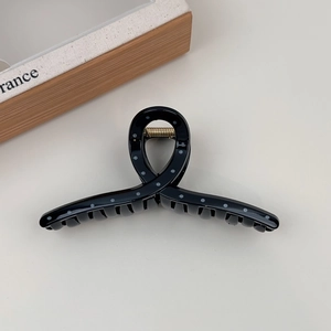 Detailed close-up of large black hair claw clip with white polka dots and metal spring