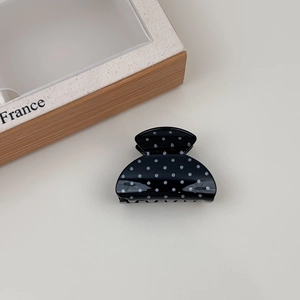 Detail of a black and white polka dot resin hair claw clip next to a wooden frame