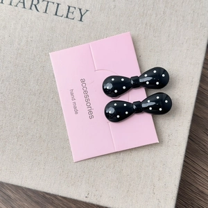Detail of two French style black and white polka dot bow hair clips on pink card